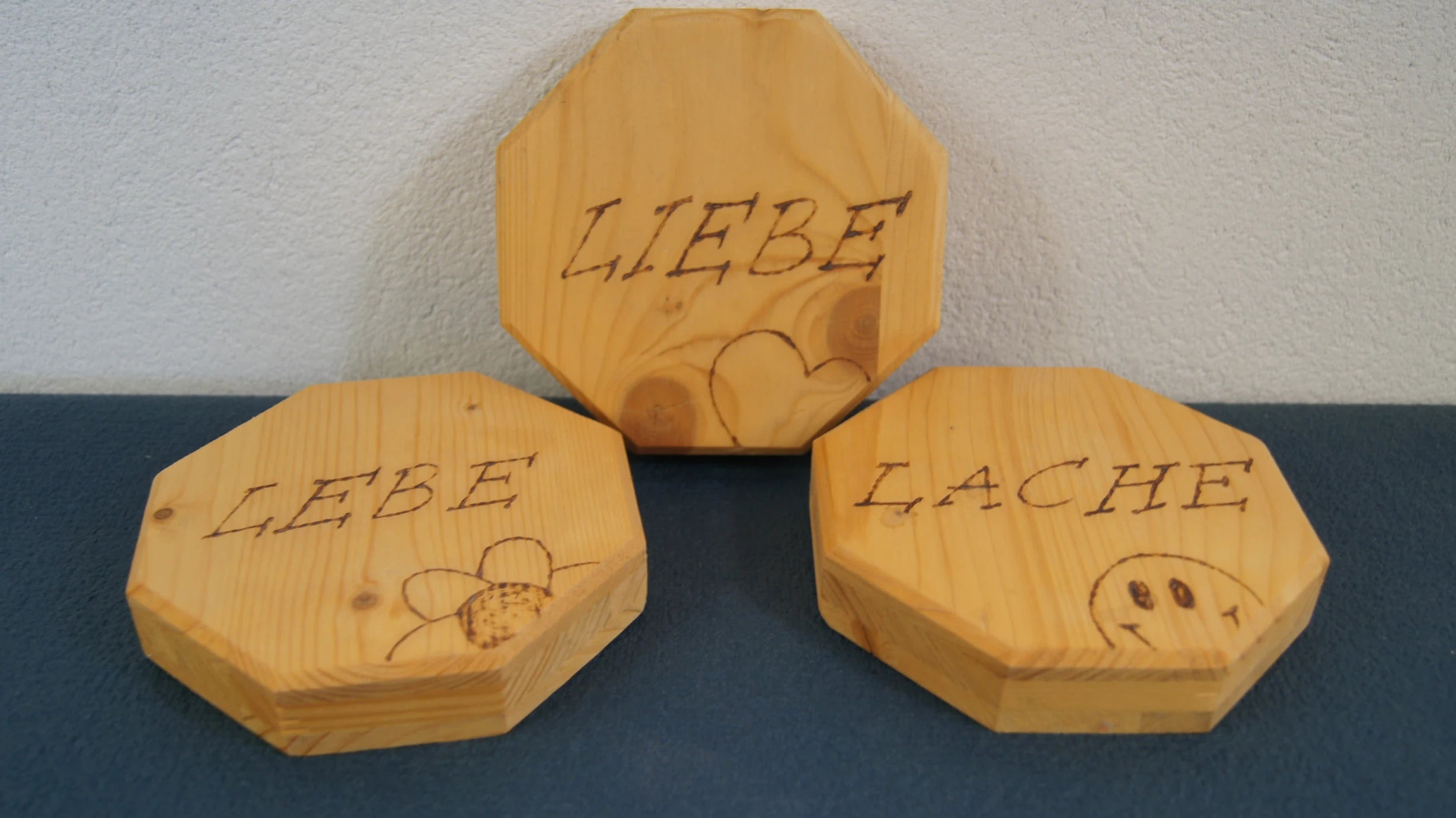 LEÑA Kunsthandwerk: Drei achteckige Holzschilder mit Brandmalerei, Made in Austria. Beschriftet mit LEBE, LIEBE, LACHE