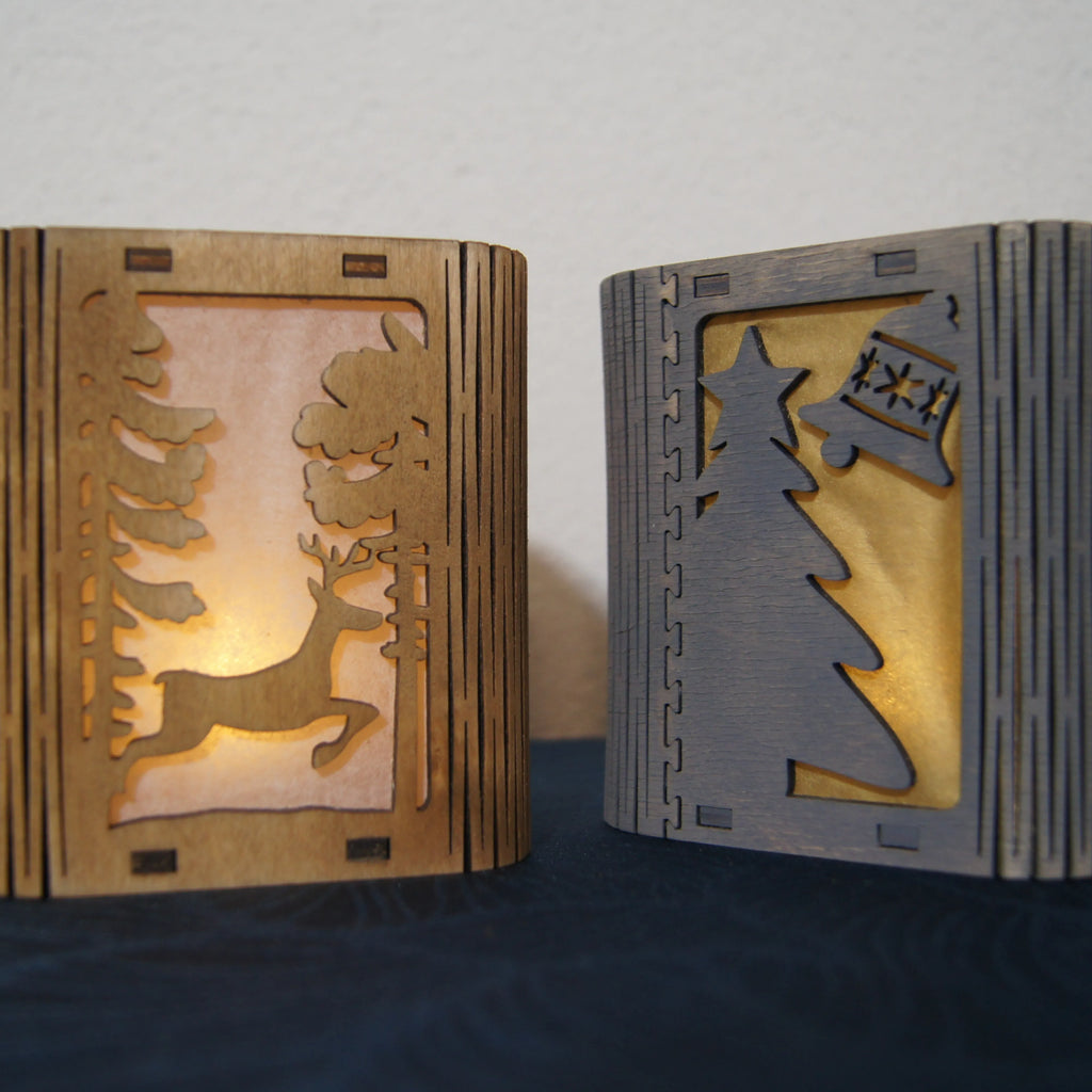 LEÑA Kunsthandwerk Holz-Laterne mit LED Licht, Made in Austria. Eine Laterne zeigt einen Hirsch, die andere einen Baum und eine Glocke